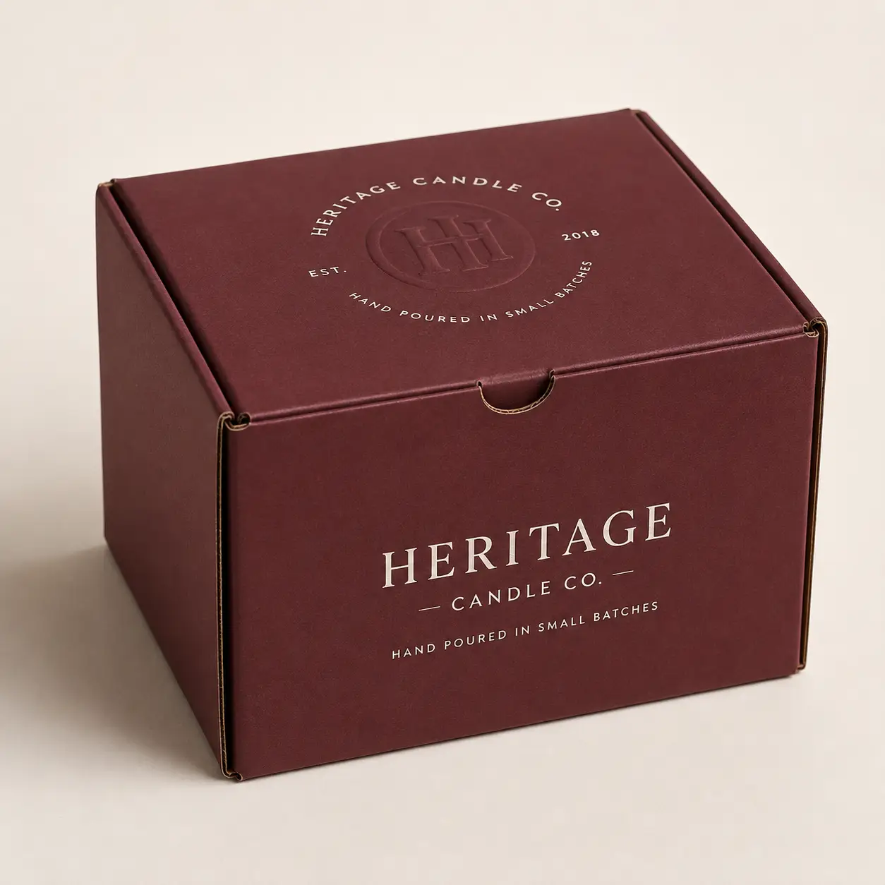 Burgundy Heritage Candle Co mailer box with embossed logo, gold typography, small batch branding, premium custom packaging design