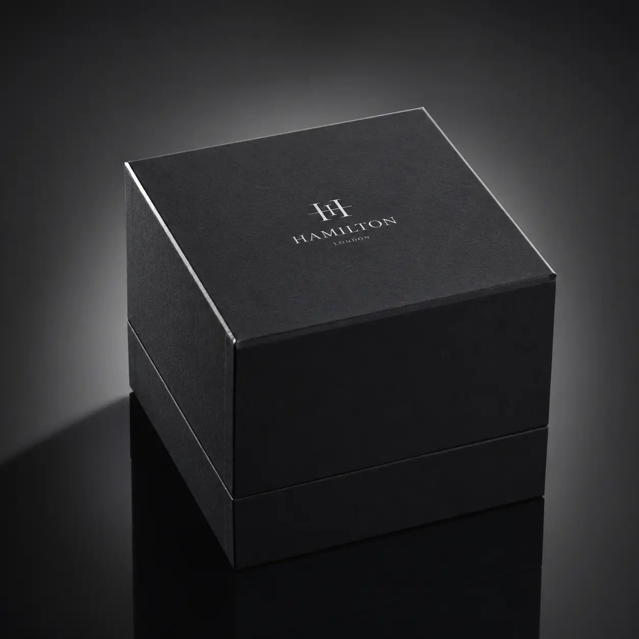 Luxury matte black Hamilton London watch gift box with silver logo, dramatic studio lighting on reflective surface