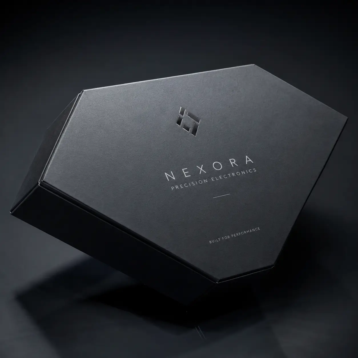 Hexagonal matte black luxury electronics box with silver Nexora Precision Electronics logo, premium custom packaging design, dark moody background