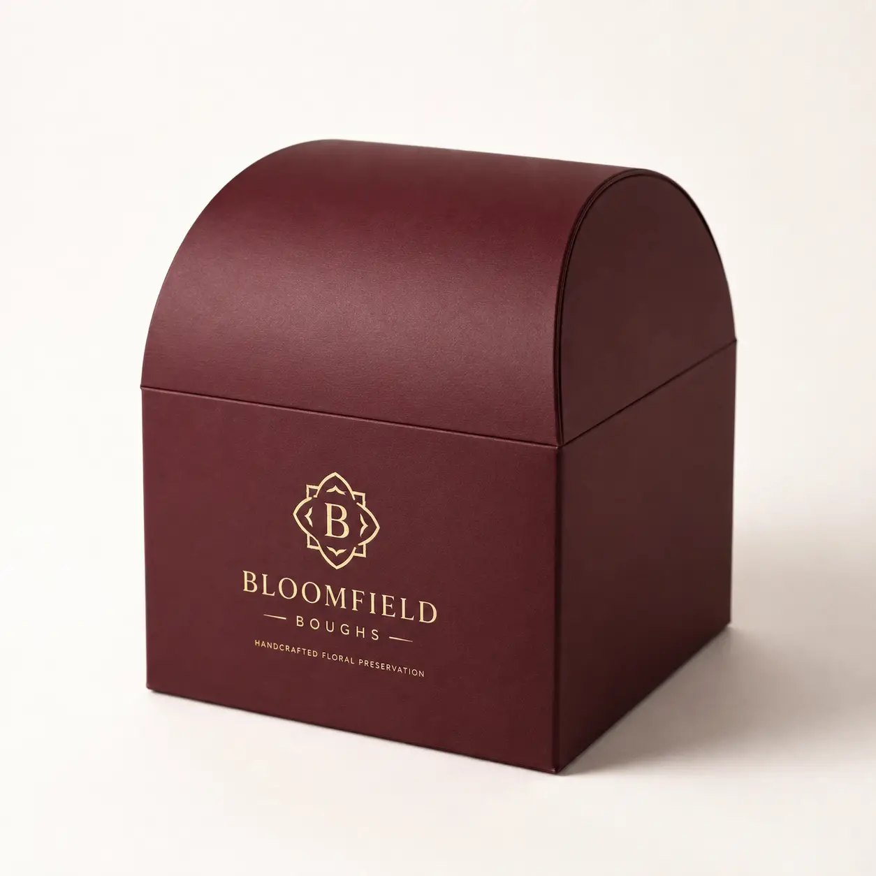 Luxury burgundy dome-top gift box with gold foil Bloomfield Boughs floral preservation branding on cream background