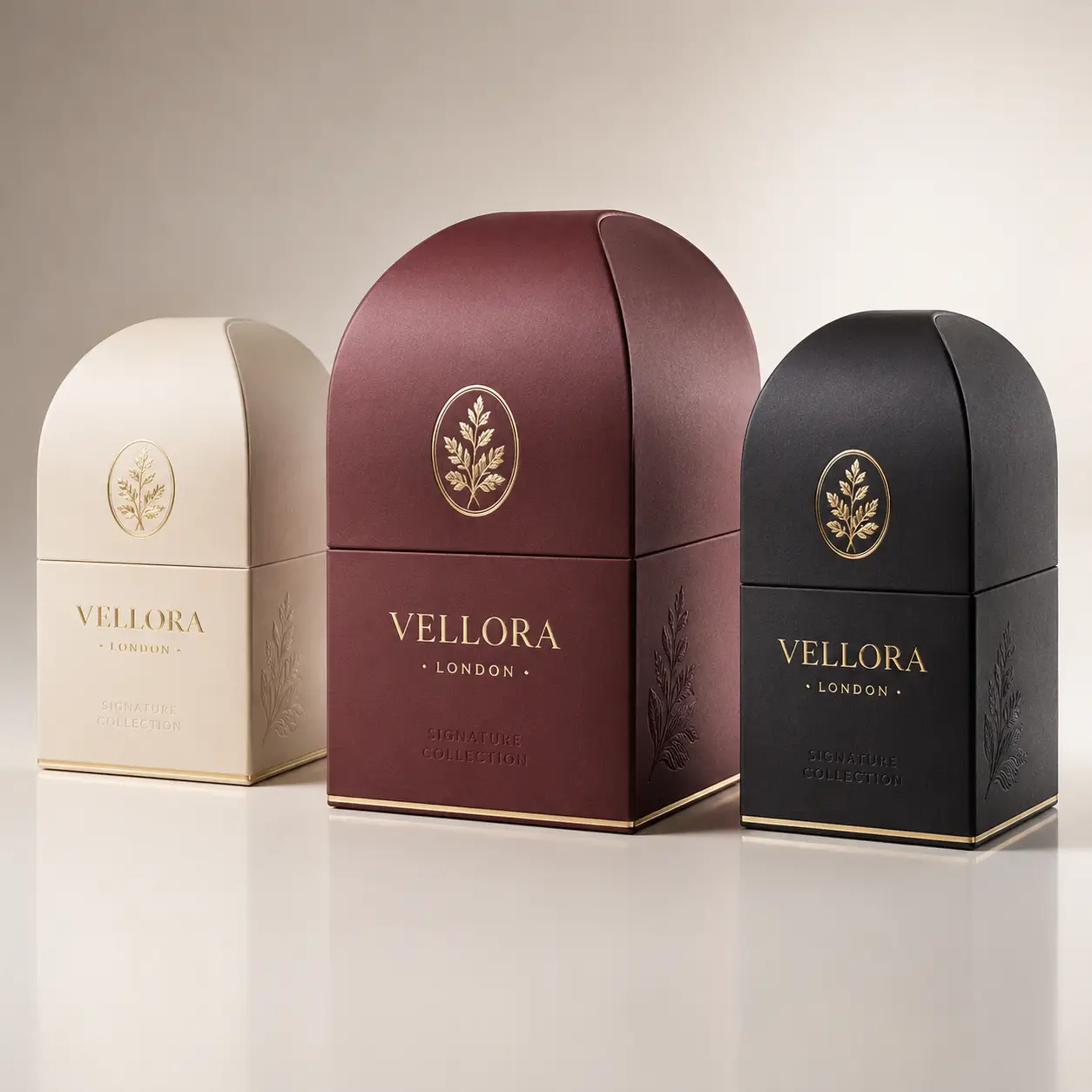 Three Vellora London Signature Collection luxury perfume boxes in cream, burgundy, and black with gold botanical embossing