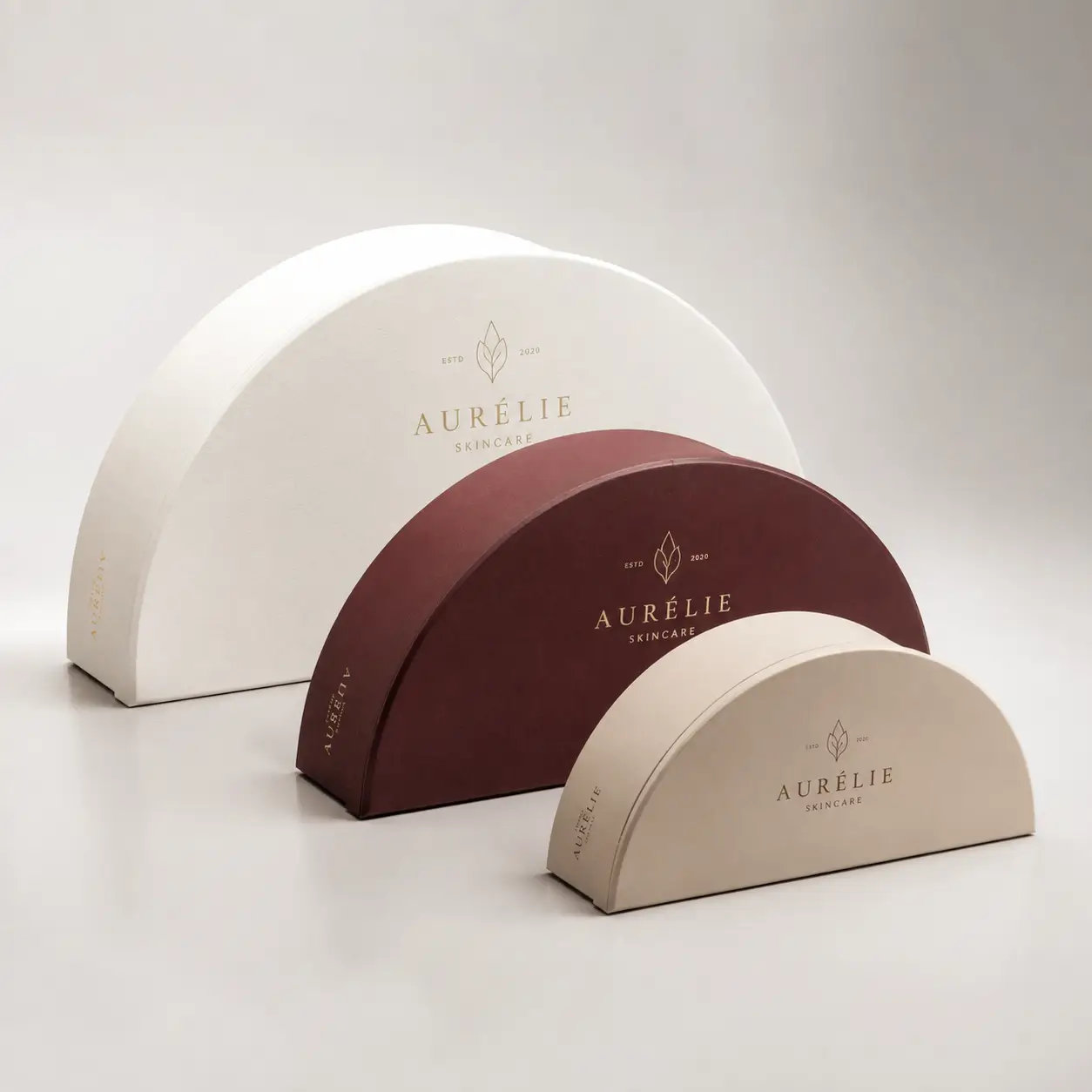 Three luxury semicircle Aurélie Skincare gift boxes in white, burgundy, and beige with gold foil branding, elegant custom packaging design