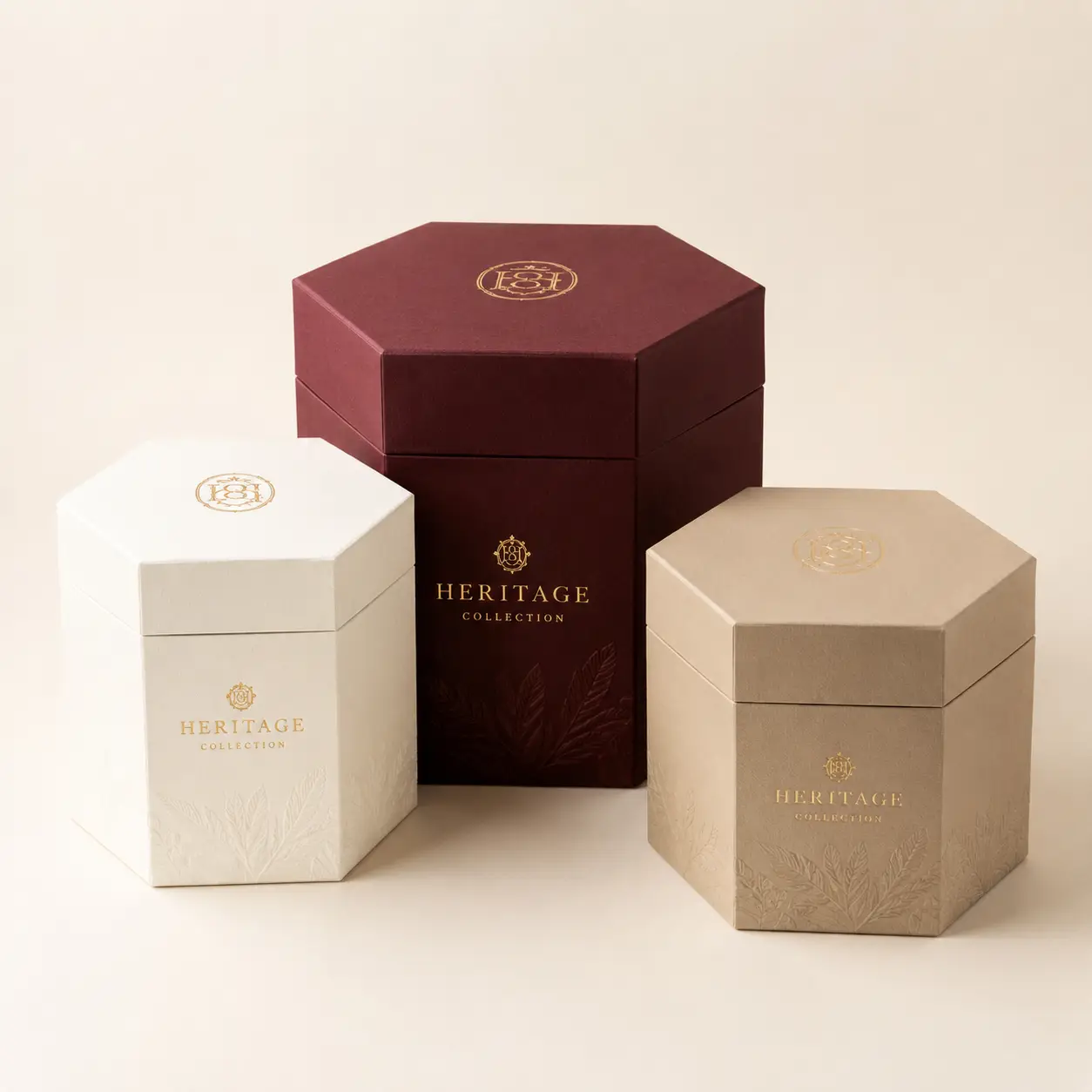 Three luxury hexagonal gift boxes in burgundy, ivory, and champagne with gold Heritage Collection branding and embossed floral designs