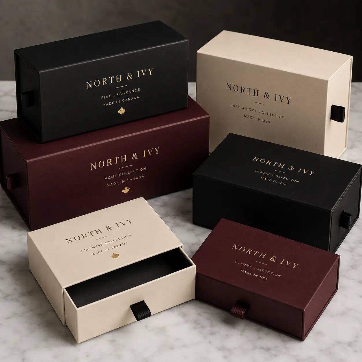 Luxury North & Ivy gift boxes in black, cream, and burgundy with gold foil branding on marble surface