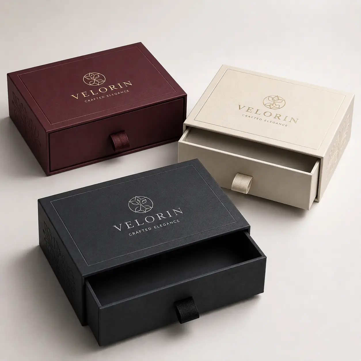 Three luxury drawer gift boxes by Velorin in black, burgundy, and cream with gold foil logo, premium rigid packaging design