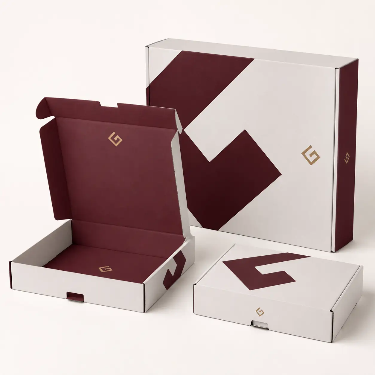 Three white and burgundy custom mailer boxes with gold G logo in different sizes, premium branded packaging design