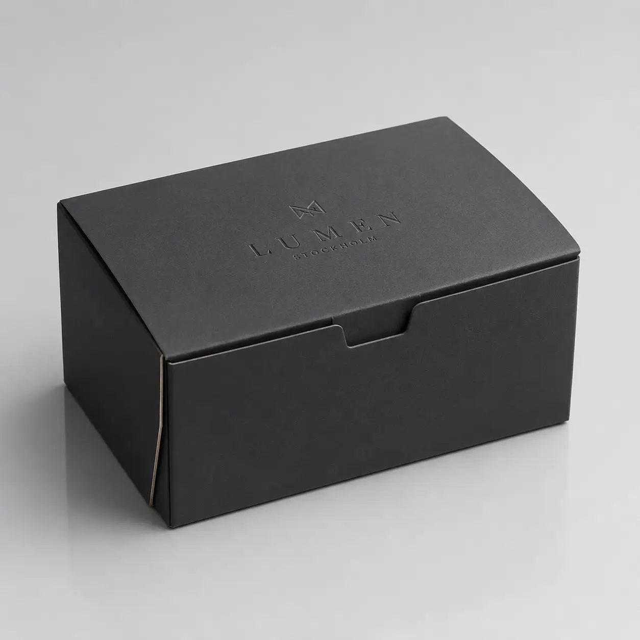 Matte black luxury gift box with embossed Lumen Stockholm logo, elegant premium packaging design on gray background