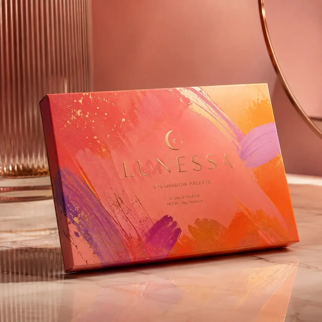 Lunessa 12-shade eyeshadow palette box with vibrant red, orange, purple brushstroke design and gold foil accents on marble surface