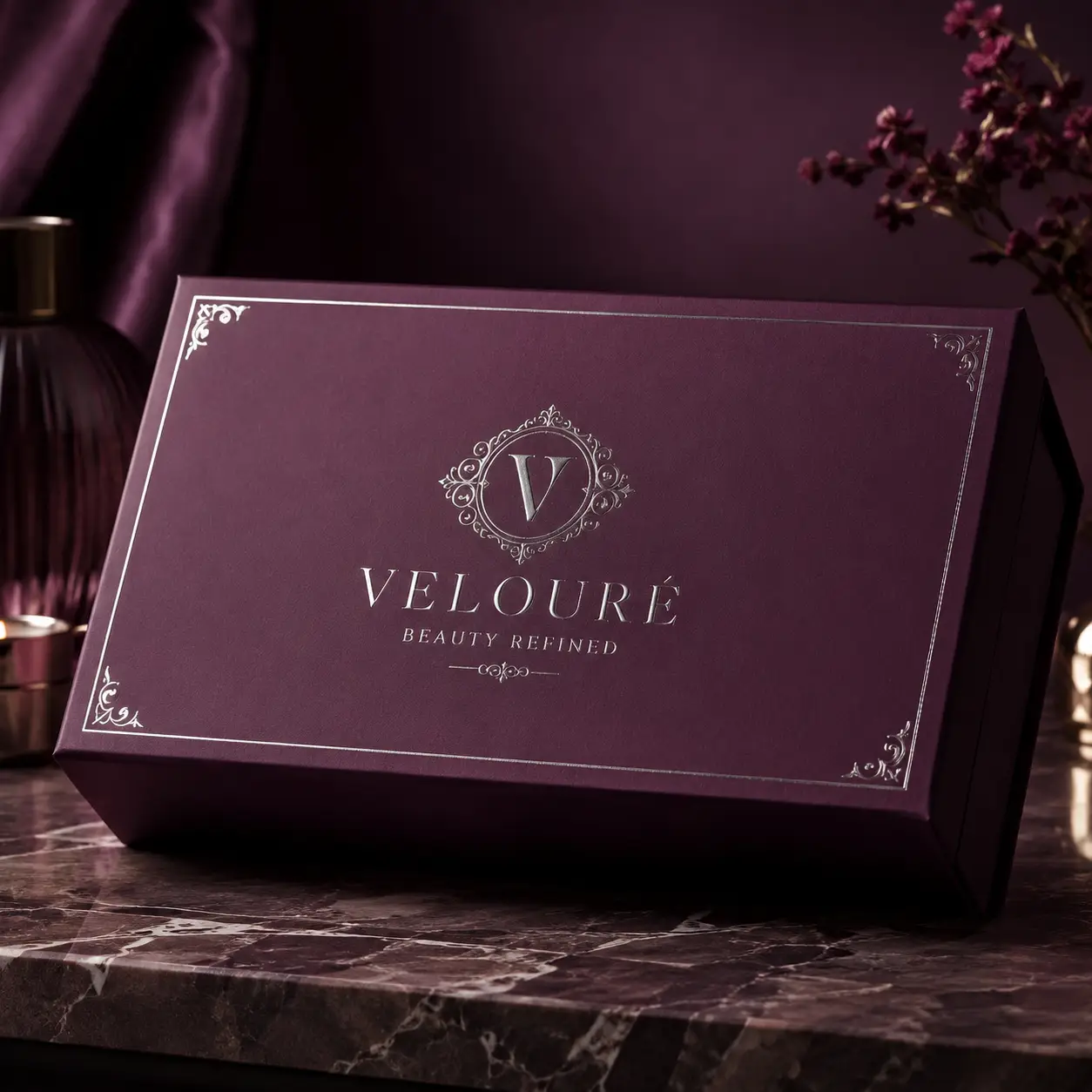 Velouré Beauty Refined luxury gift box in deep plum with silver foil logo on marble surface, elegant premium packaging design
