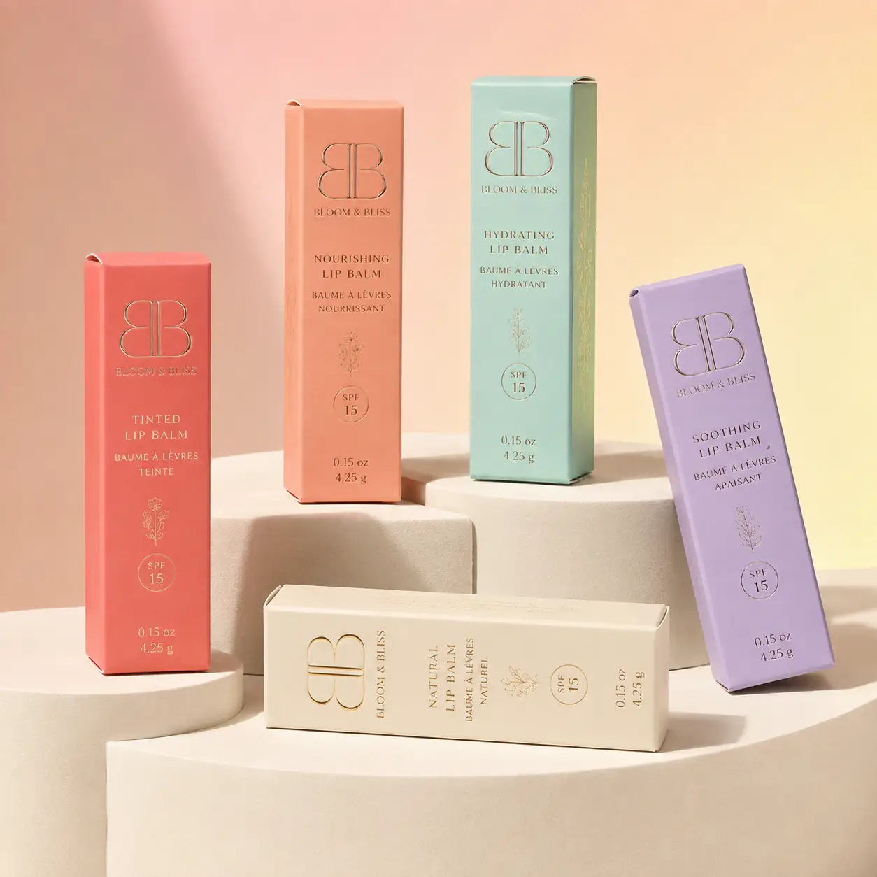 Five Bloom & Bliss lip balm boxes in pink, peach, mint, white, and lavender with SPF 15 on cream pedestals