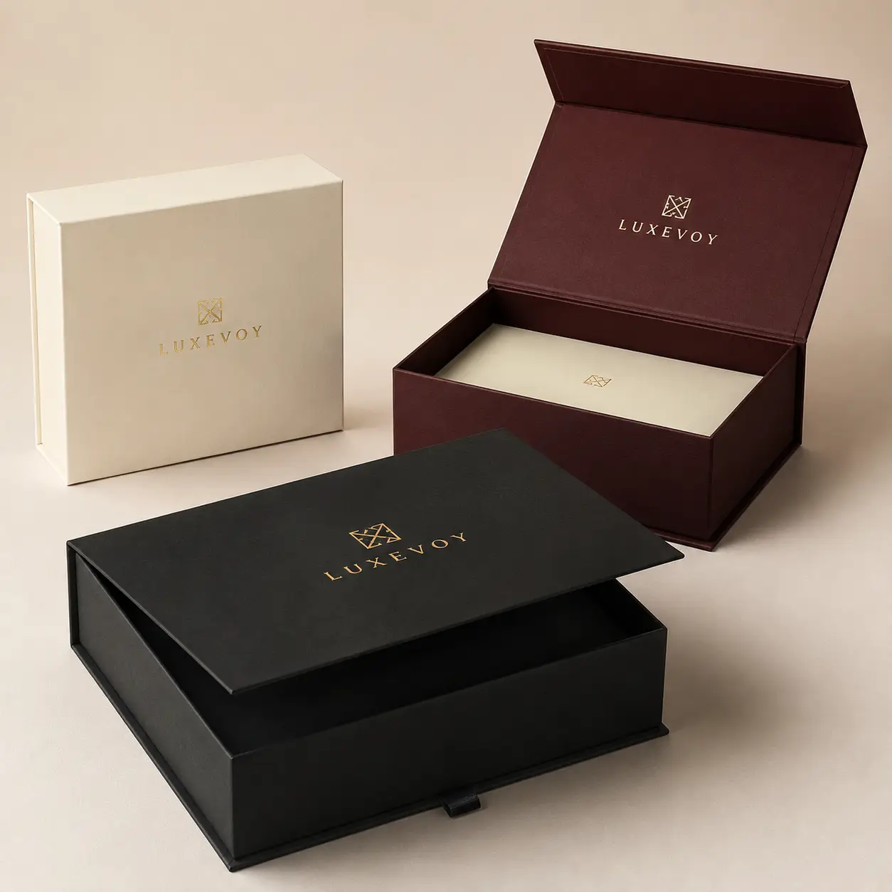 Three luxury rigid gift boxes by Luxevoy in black, burgundy, and ivory with gold foil logo branding for premium packaging
