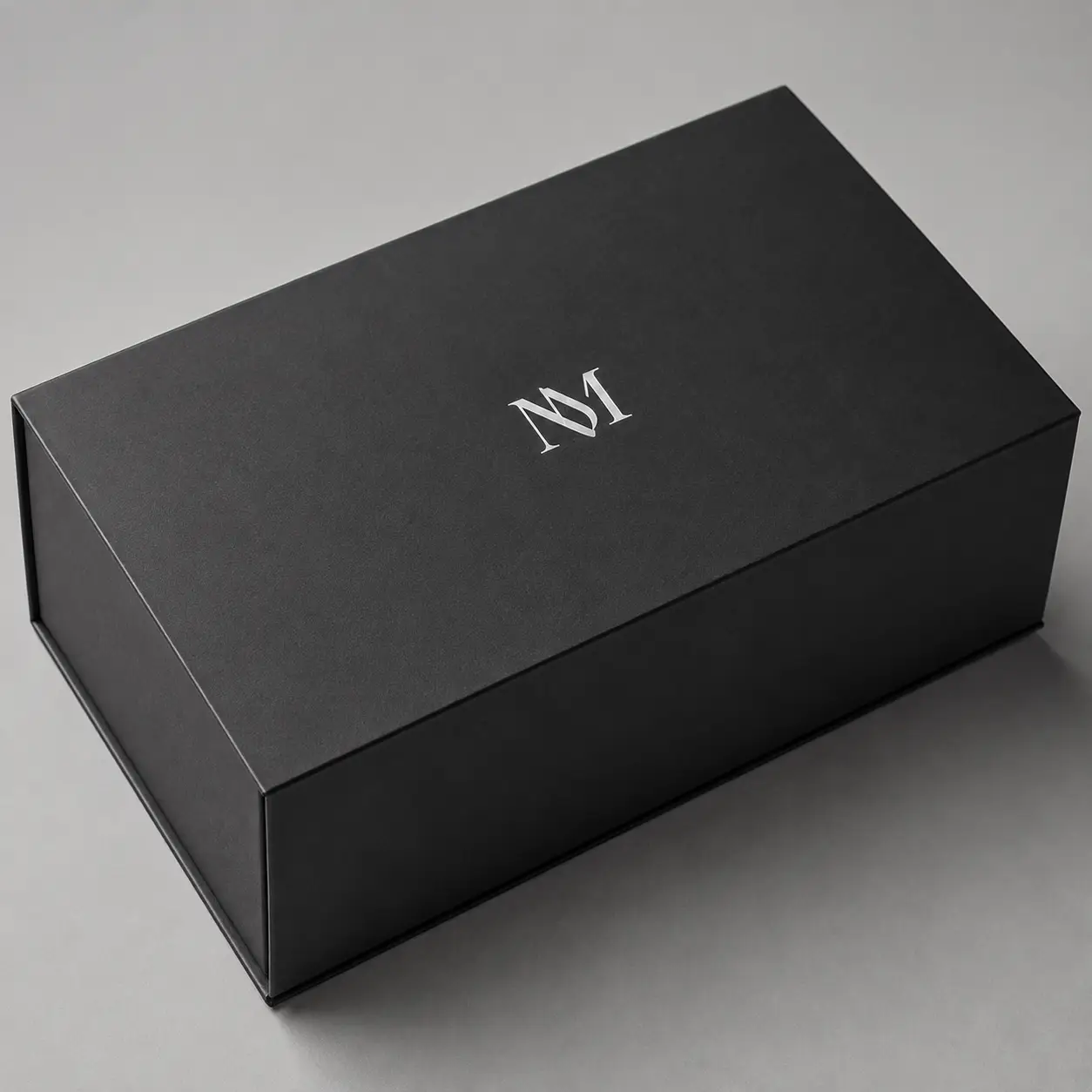 Luxury matte black magnetic gift box with silver NM monogram logo, premium custom packaging by The Packaging Masters