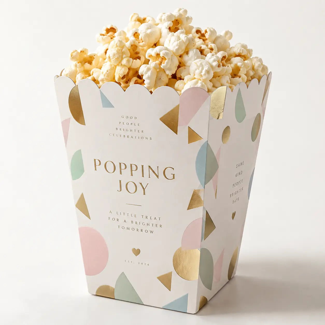Elegant white popcorn box with gold, pink, mint confetti shapes, filled with fresh popcorn, branded Popping Joy Est. 2024 packaging
