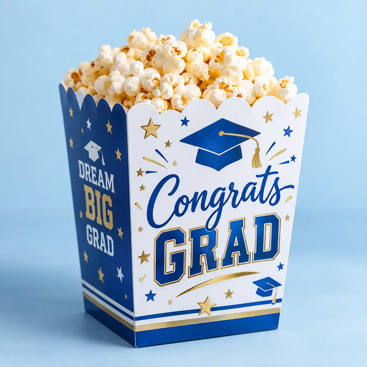 Blue and white graduation popcorn box printed with Congrats Grad and Dream Big Grad, filled with popcorn, gold star accents