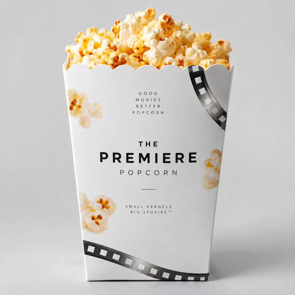 White cinema-themed popcorn box packaging design with film strip, bold black text reading The Premiere Popcorn, filled with fresh buttery popcorn