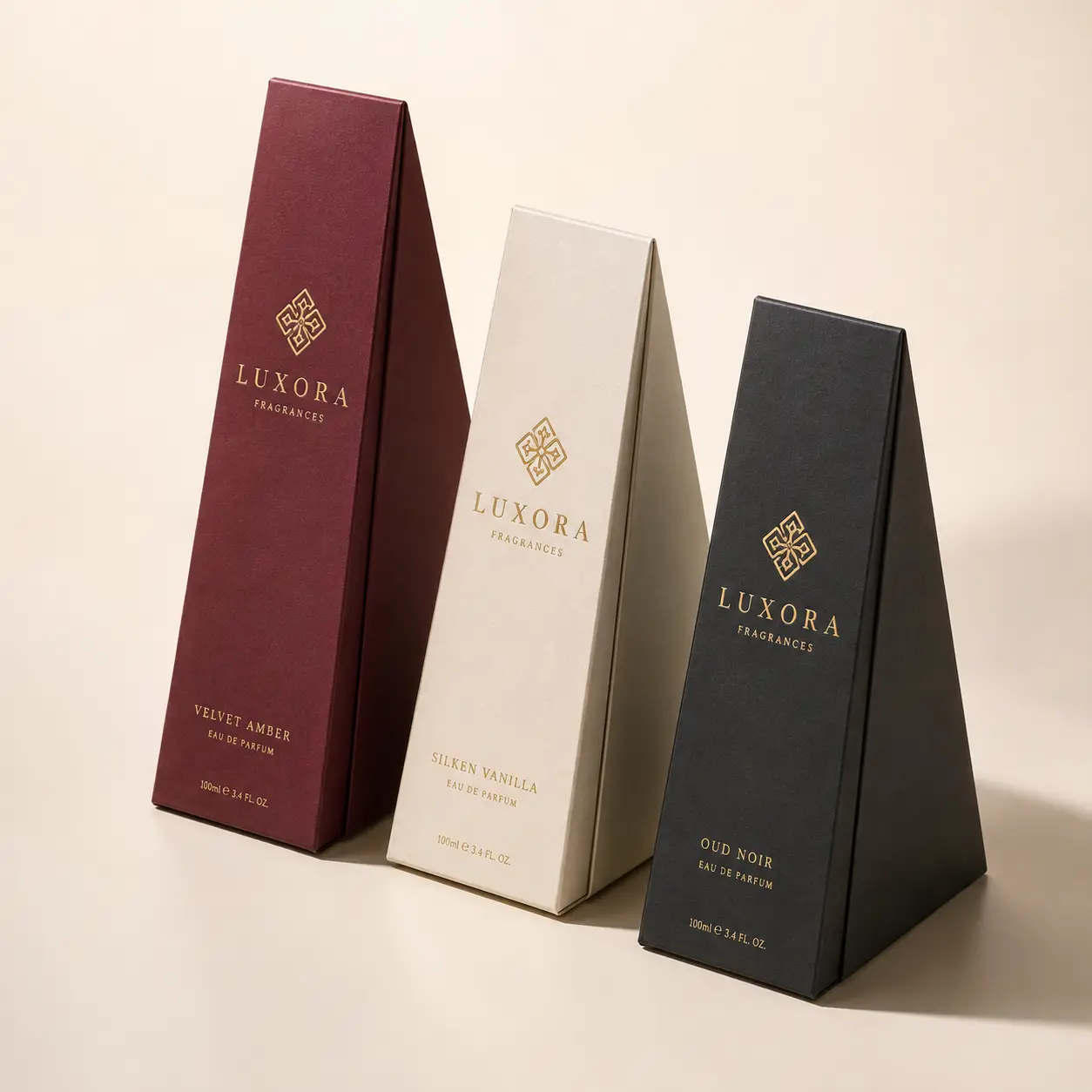 Three Luxora Fragrances luxury perfume boxes in burgundy, cream, and black with gold foil branding, triangular elegant packaging design