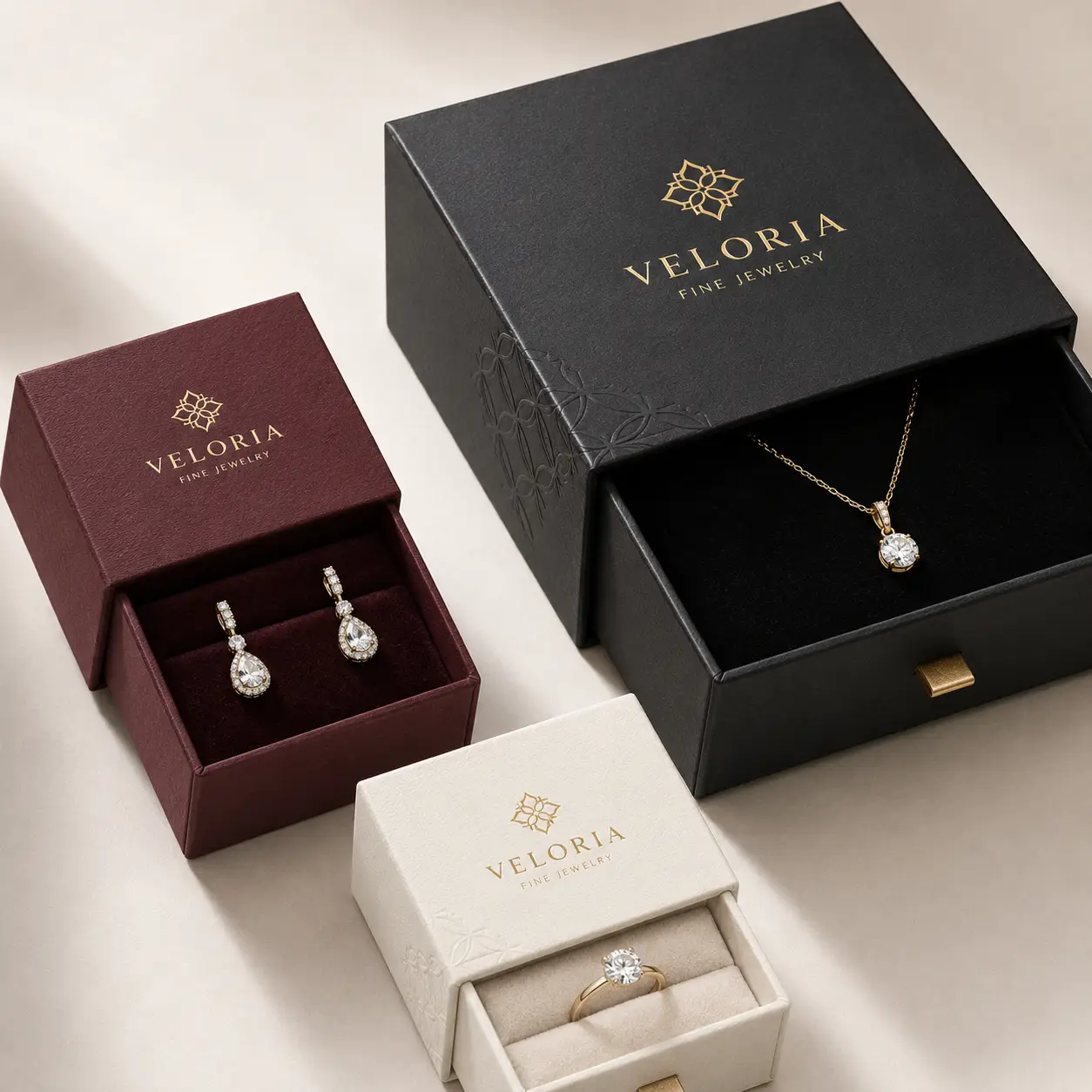 Veloria Fine Jewelry luxury packaging set featuring black drawer box, burgundy earring box, and cream ring box with gold logo