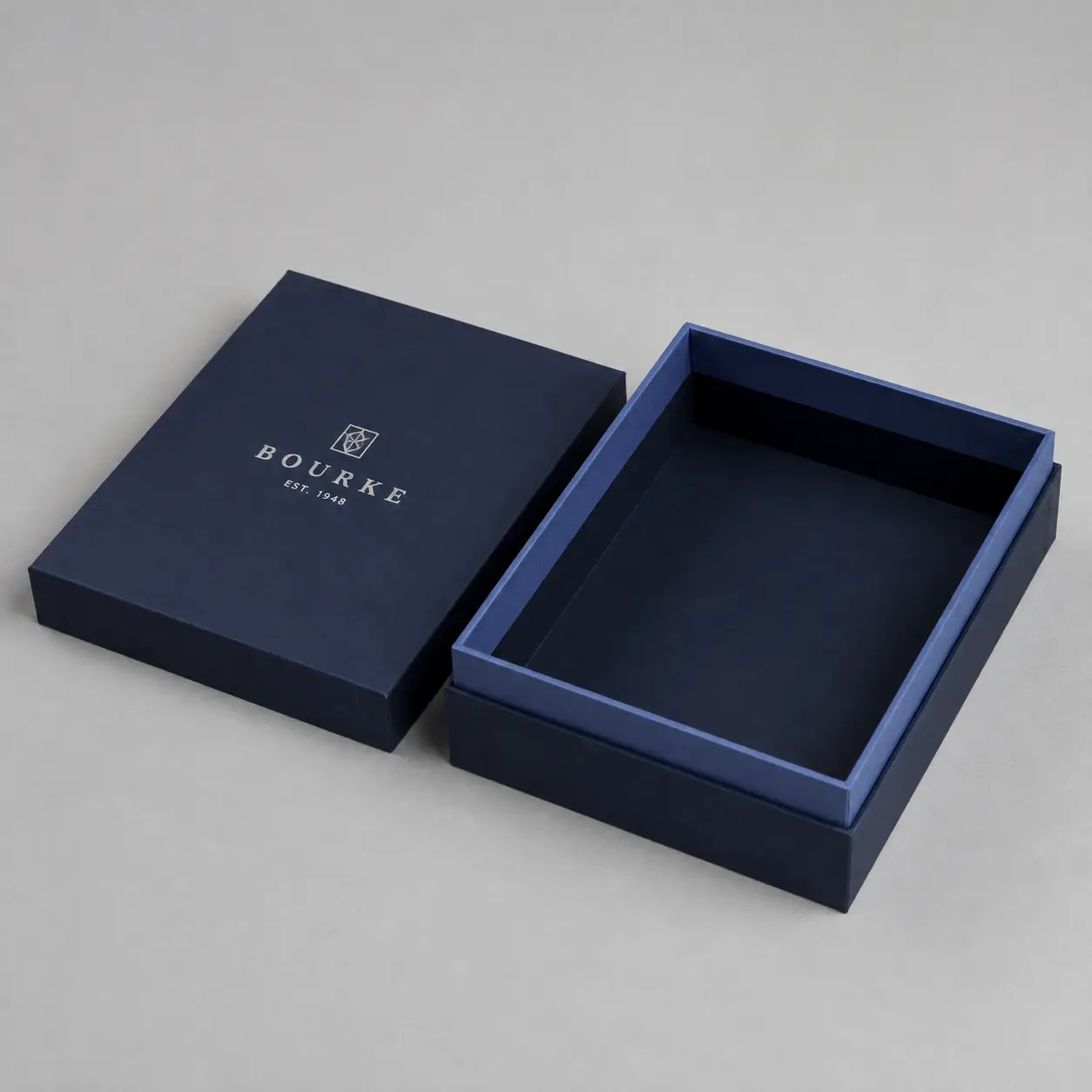 Navy blue luxury gift box with silver Bourke Est. 1948 logo, open lid beside base, premium rigid packaging on gray background