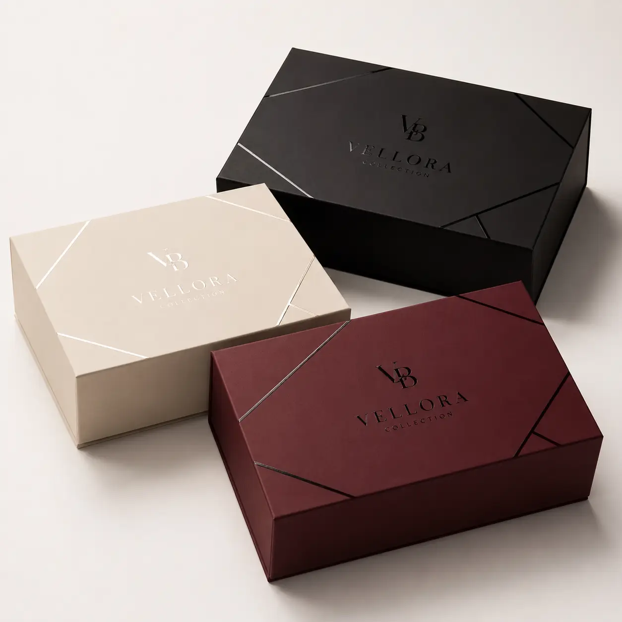 Three luxury Vellora Collection gift boxes in black, cream, and burgundy with geometric foil design on white background