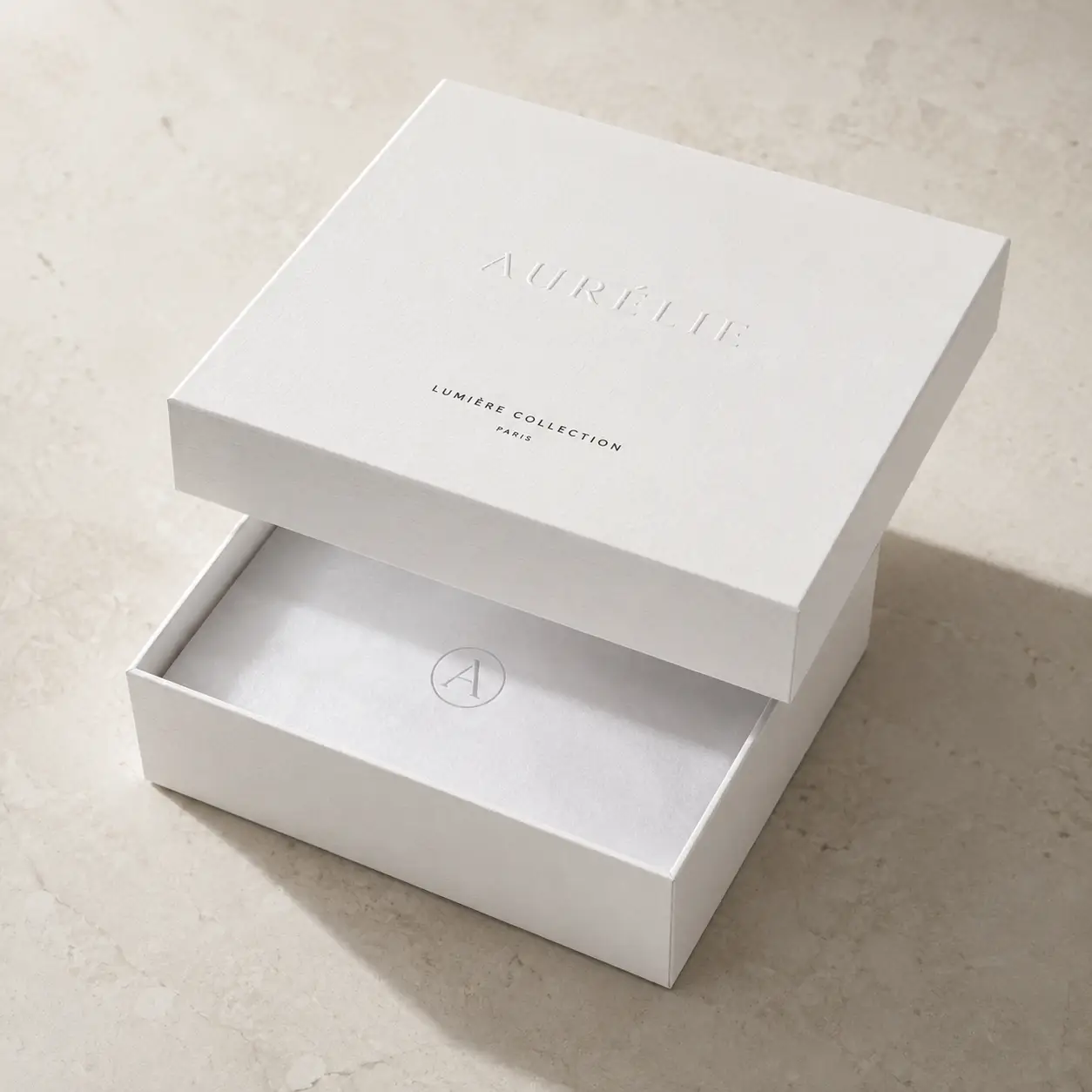 Elegant white luxury gift box with silver embossed Aurélie Lumière Collection Paris branding on marble surface