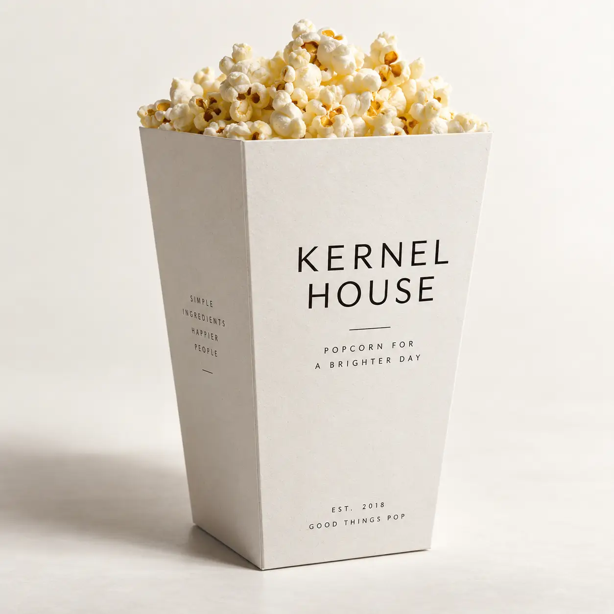 White minimalist popcorn box packaging design for Kernel House brand, filled with fresh popcorn, clean typography on light background