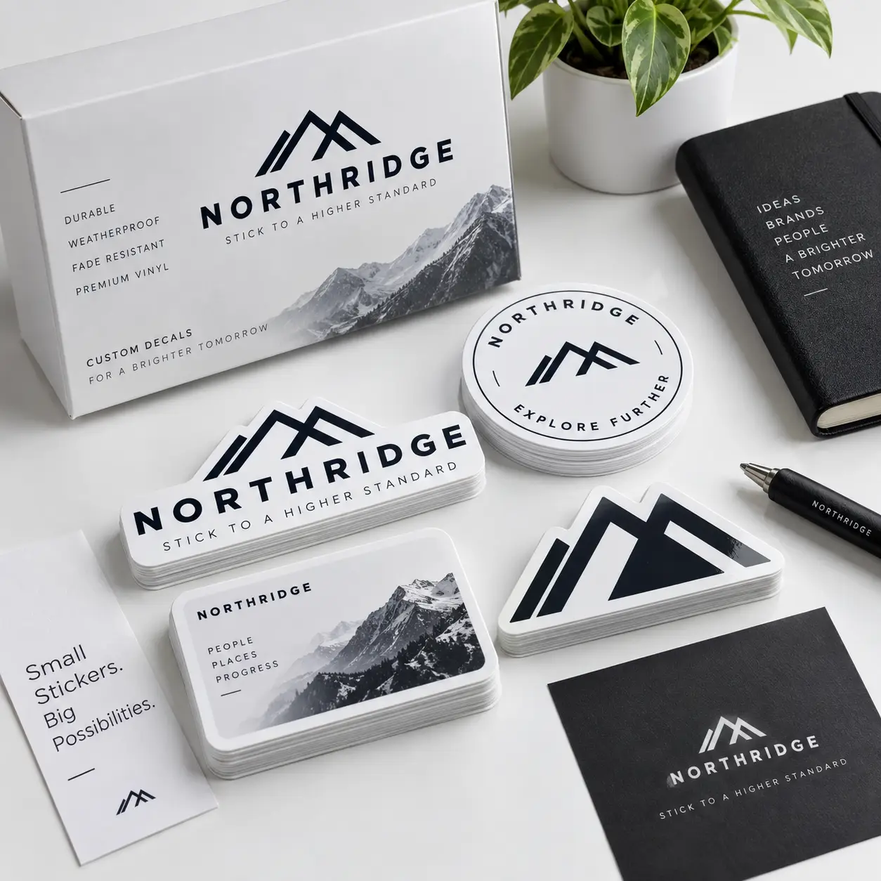 Black and white Northridge custom vinyl sticker collection with mountain logo, packaging box, round and die-cut decals on white desk