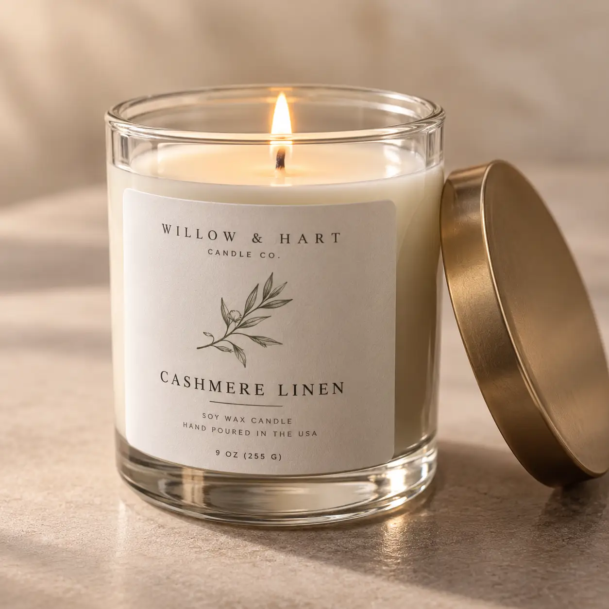 Willow & Hart Cashmere Linen soy wax candle in clear glass jar with gold lid, lit flame, elegant white label packaging