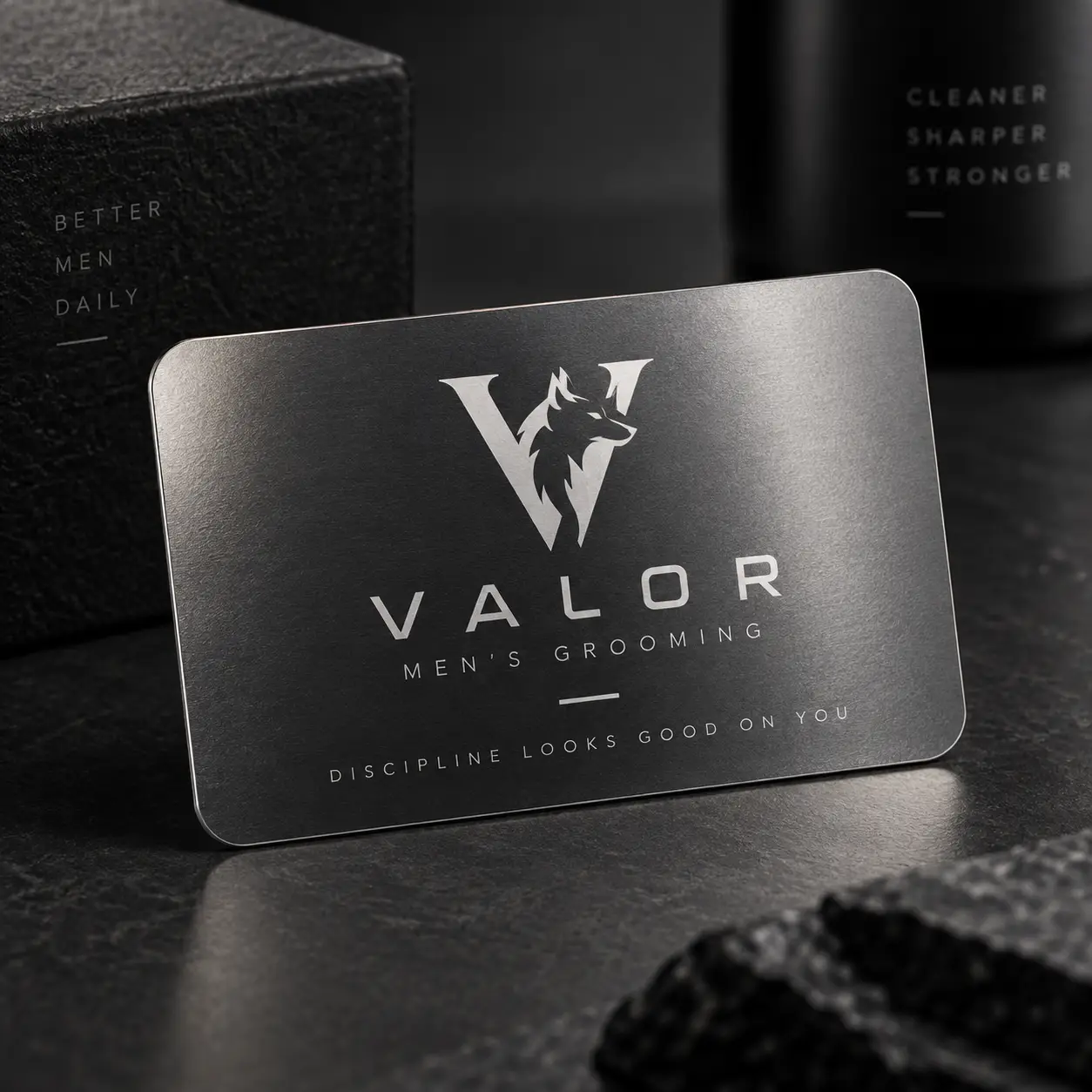 Valor Men's Grooming brushed steel metal business card with wolf logo, dark luxury packaging background, discipline looks good on you tagline