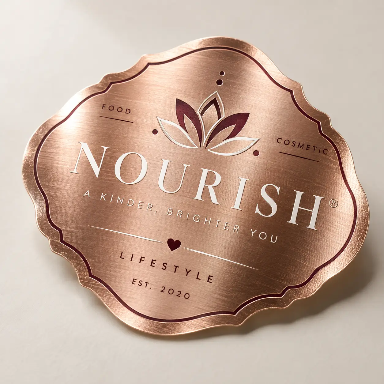 Rose gold brushed metal badge logo for Nourish lifestyle brand, featuring lotus flower, elegant scalloped edges, EST. 2020 custom packaging