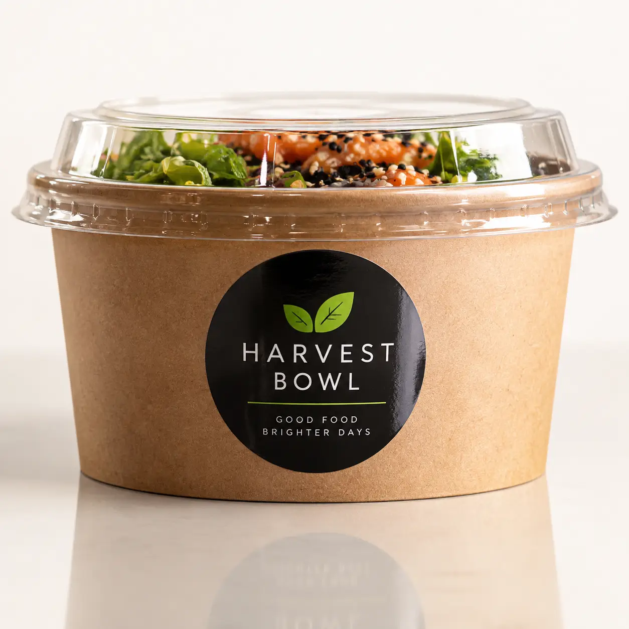 Kraft paper salad bowl with clear dome lid and black Harvest Bowl logo sticker, filled with fresh poke bowl ingredients