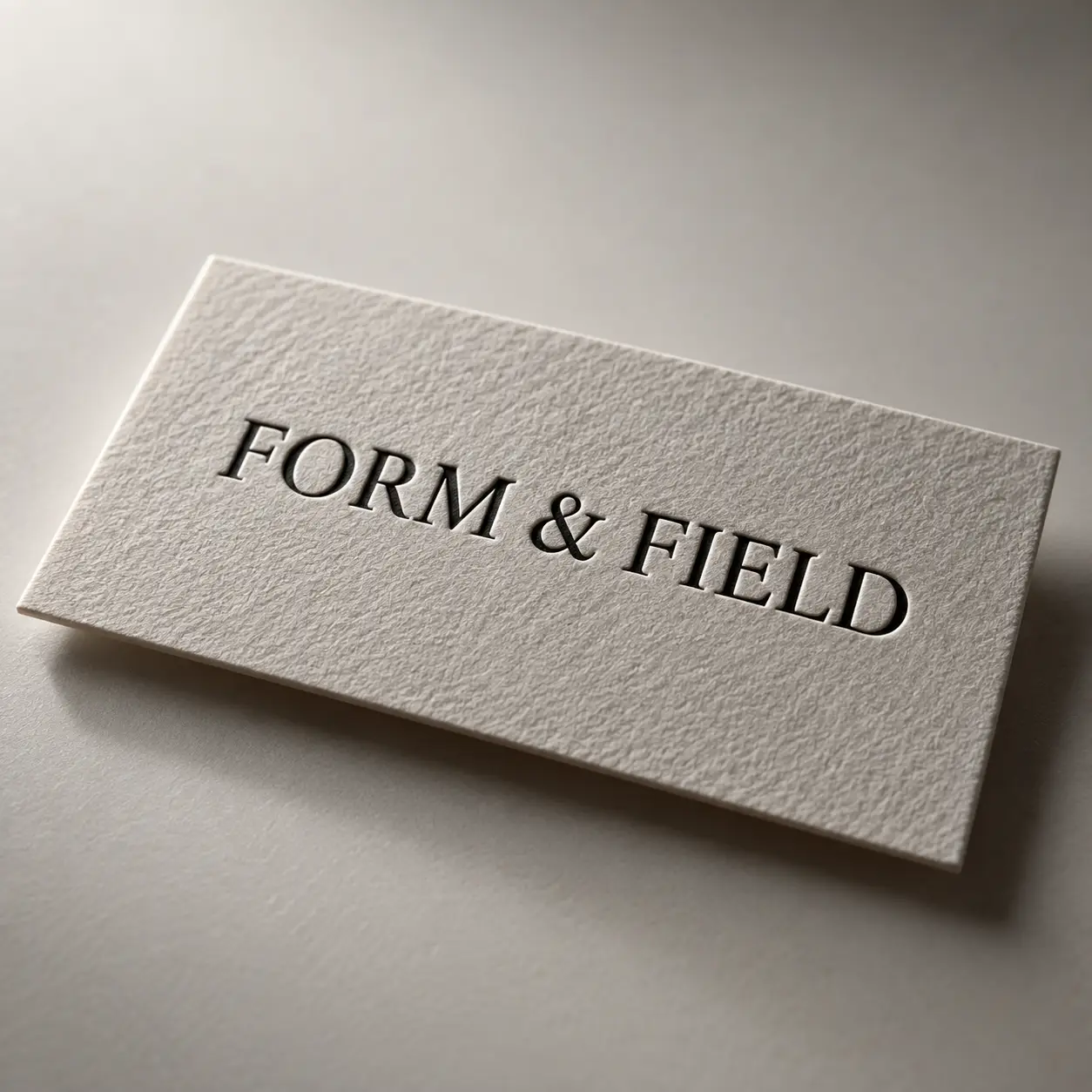 Letterpress business card on textured cream paper with embossed "FORM & FIELD" serif text, minimalist luxury packaging design