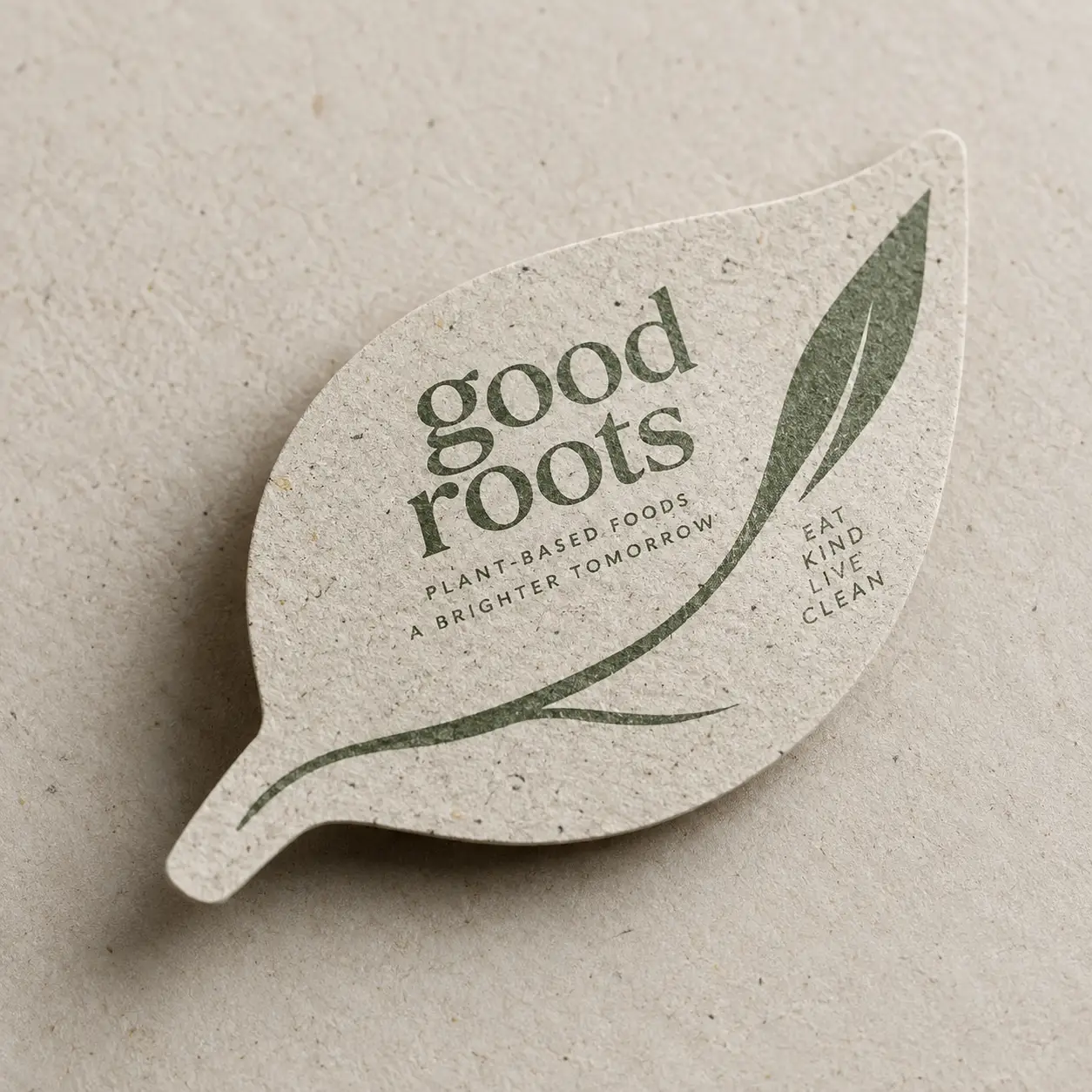 Leaf-shaped recycled cardboard packaging card for Good Roots plant-based foods brand, sage green botanical print, eco-friendly design