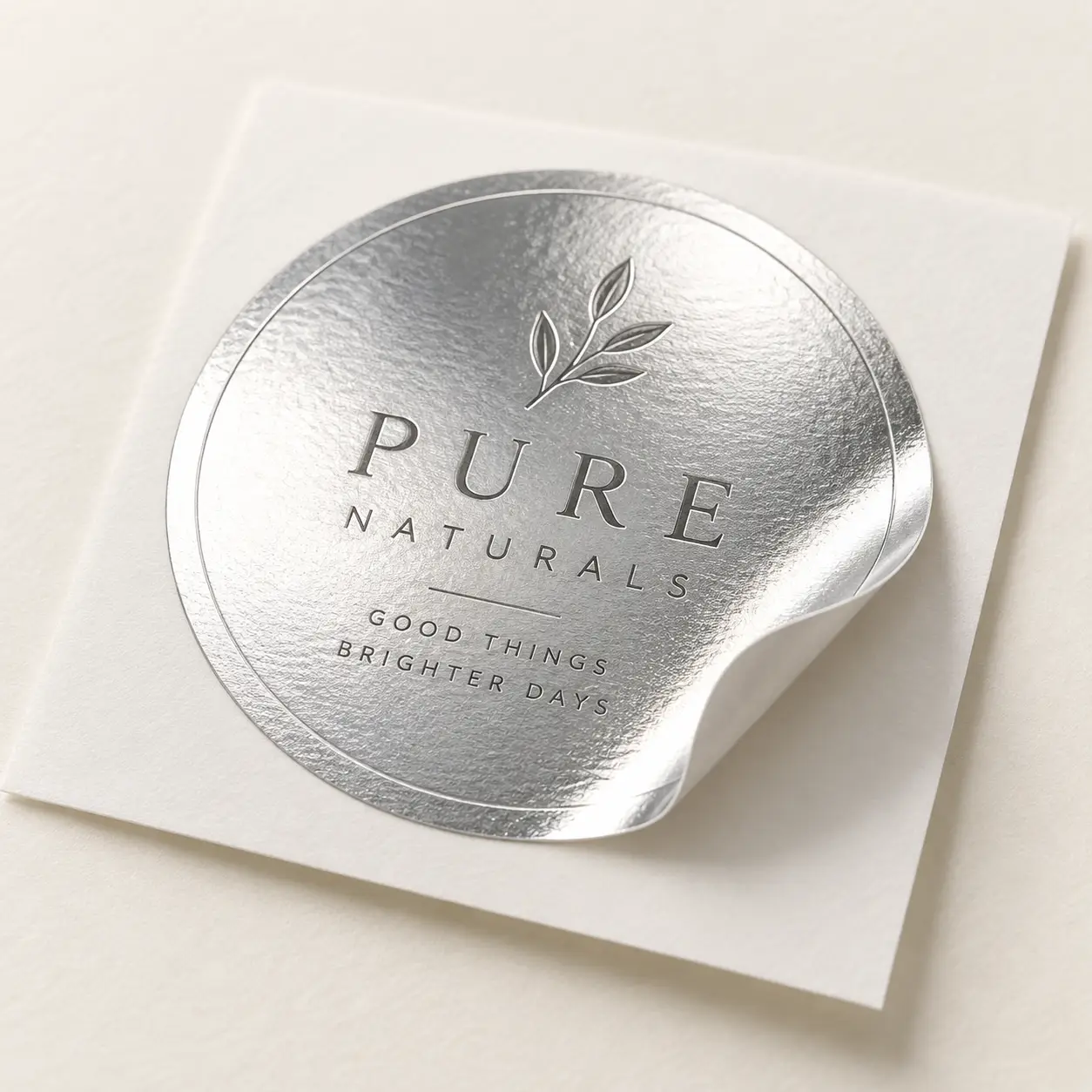 Silver foil round sticker label for Pure Naturals brand with leaf logo and tagline Good Things Brighter Days on white backing