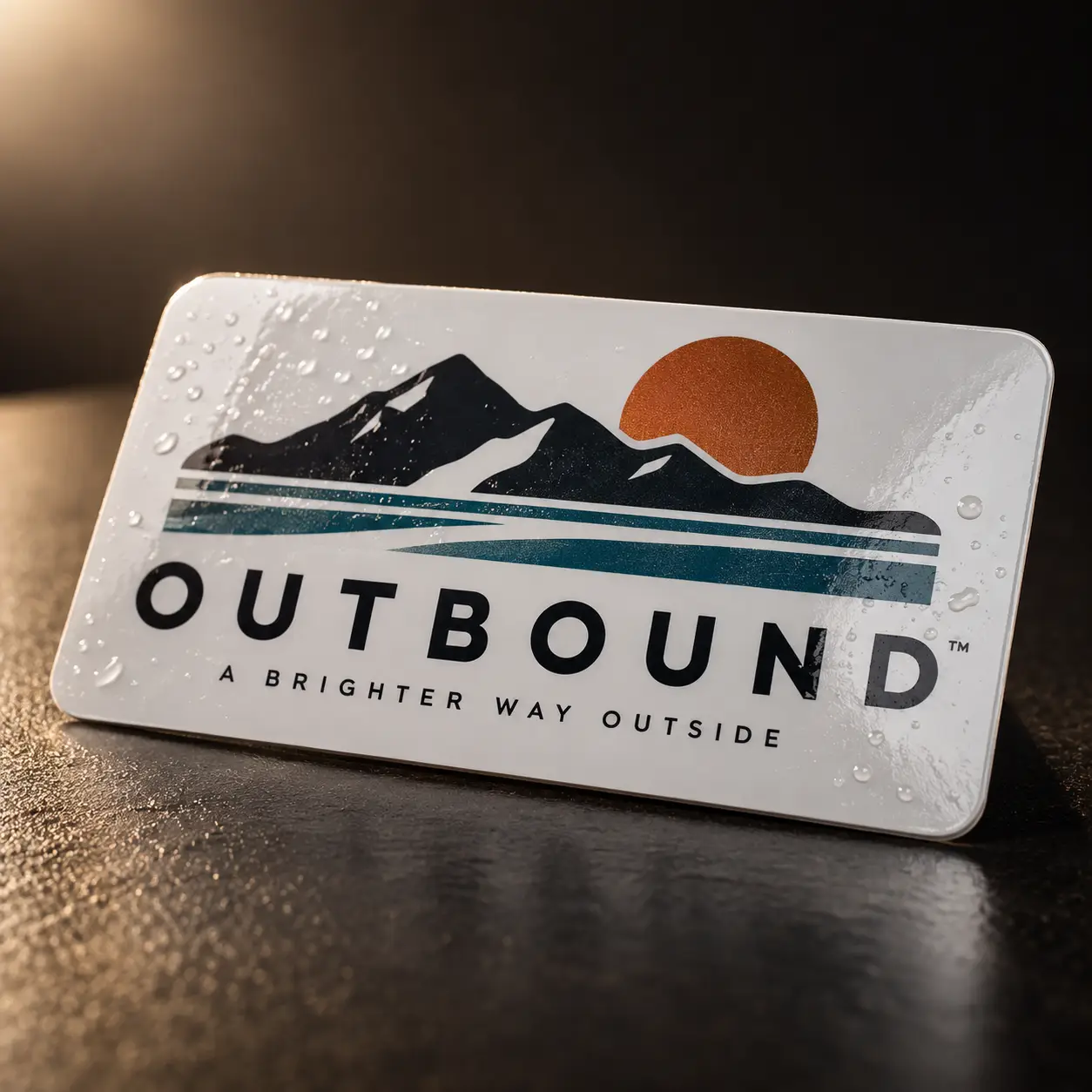 White waterproof sticker card with Outbound™ brand logo, mountain sunset design in navy, teal, and burnt orange, custom printed packaging