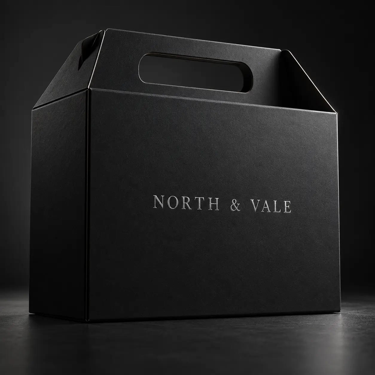 Elegant matte black gable gift box with silver embossed North & Vale logo, premium luxury packaging design on dark background