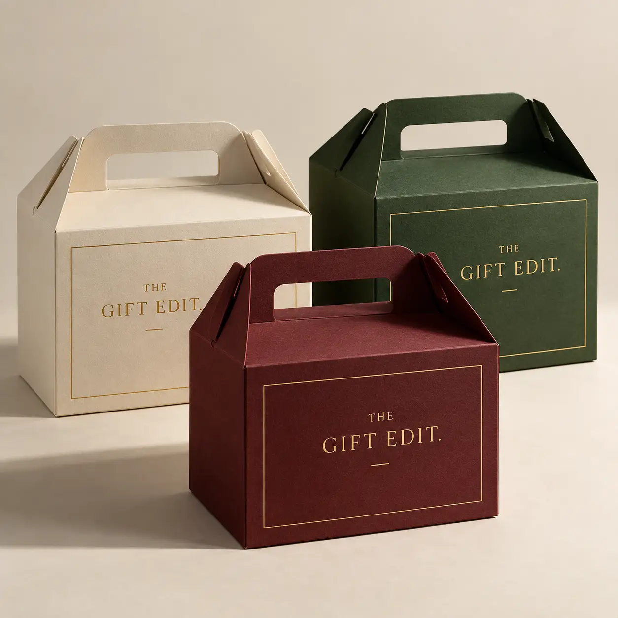 Three luxury gable gift boxes in cream, dark green, and burgundy with gold foil The Gift Edit branding, elegant packaging design