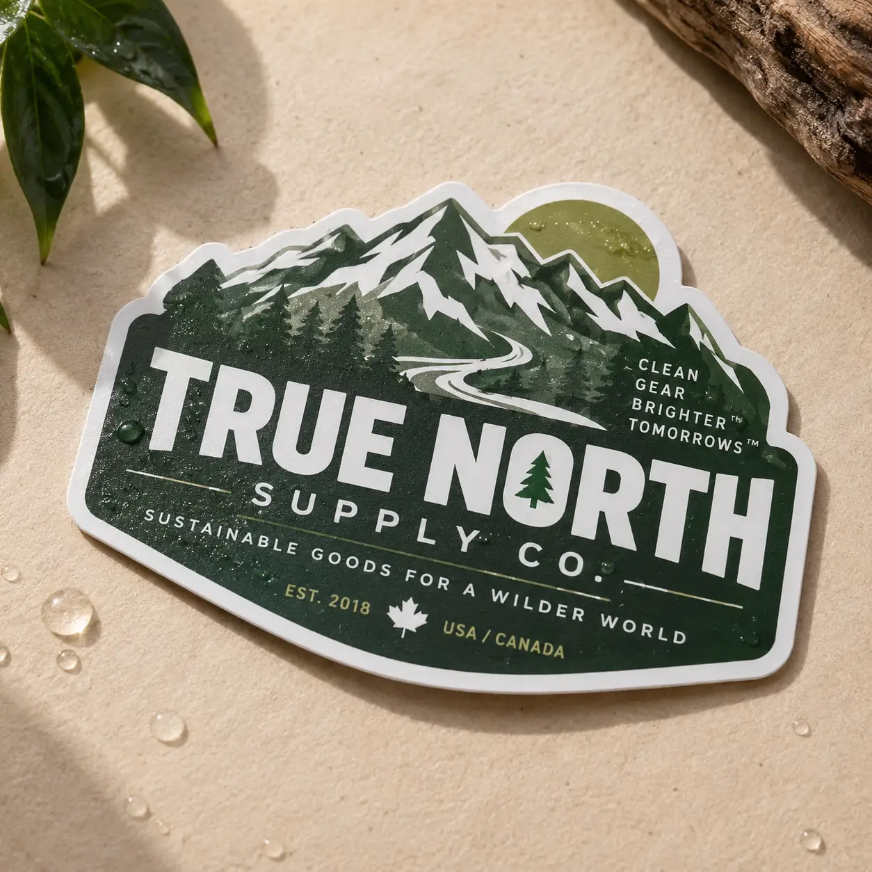 Dark green die-cut sticker for True North Supply Co. featuring mountains, pine trees, and golden sun on beige surface with water droplets