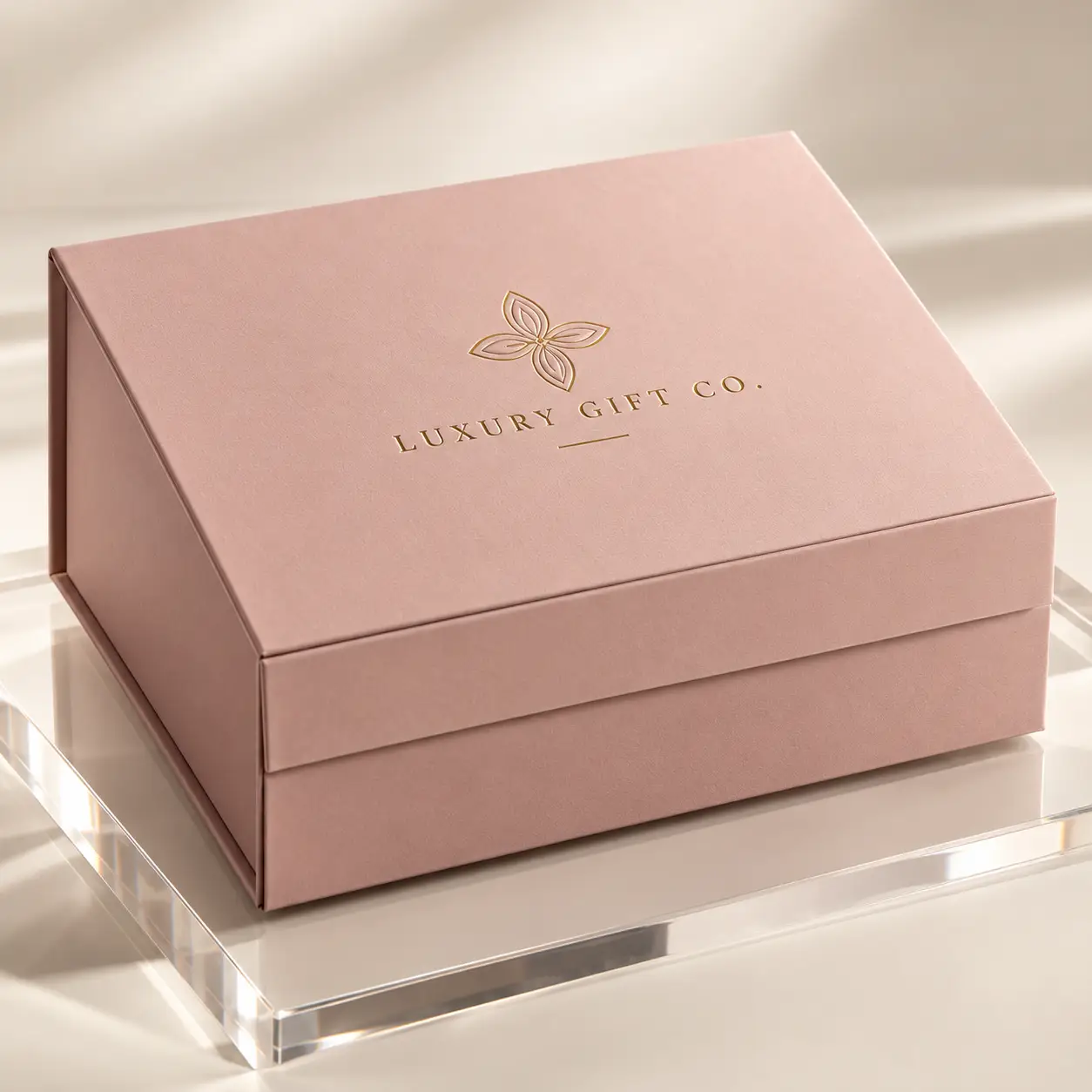 Blush pink luxury gift box with gold foil logo on acrylic stand, elegant custom packaging by The Packaging Masters