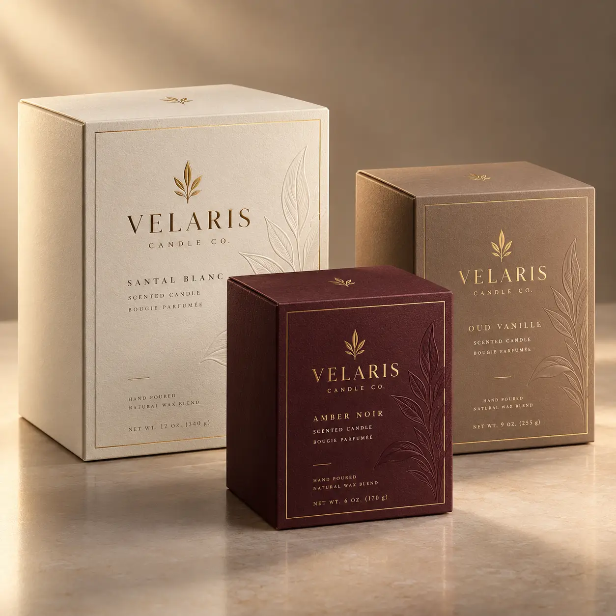 Velaris Candle Co luxury packaging trio: cream Santal Blanc, burgundy Amber Noir, taupe Oud Vanille boxes with gold foil branding