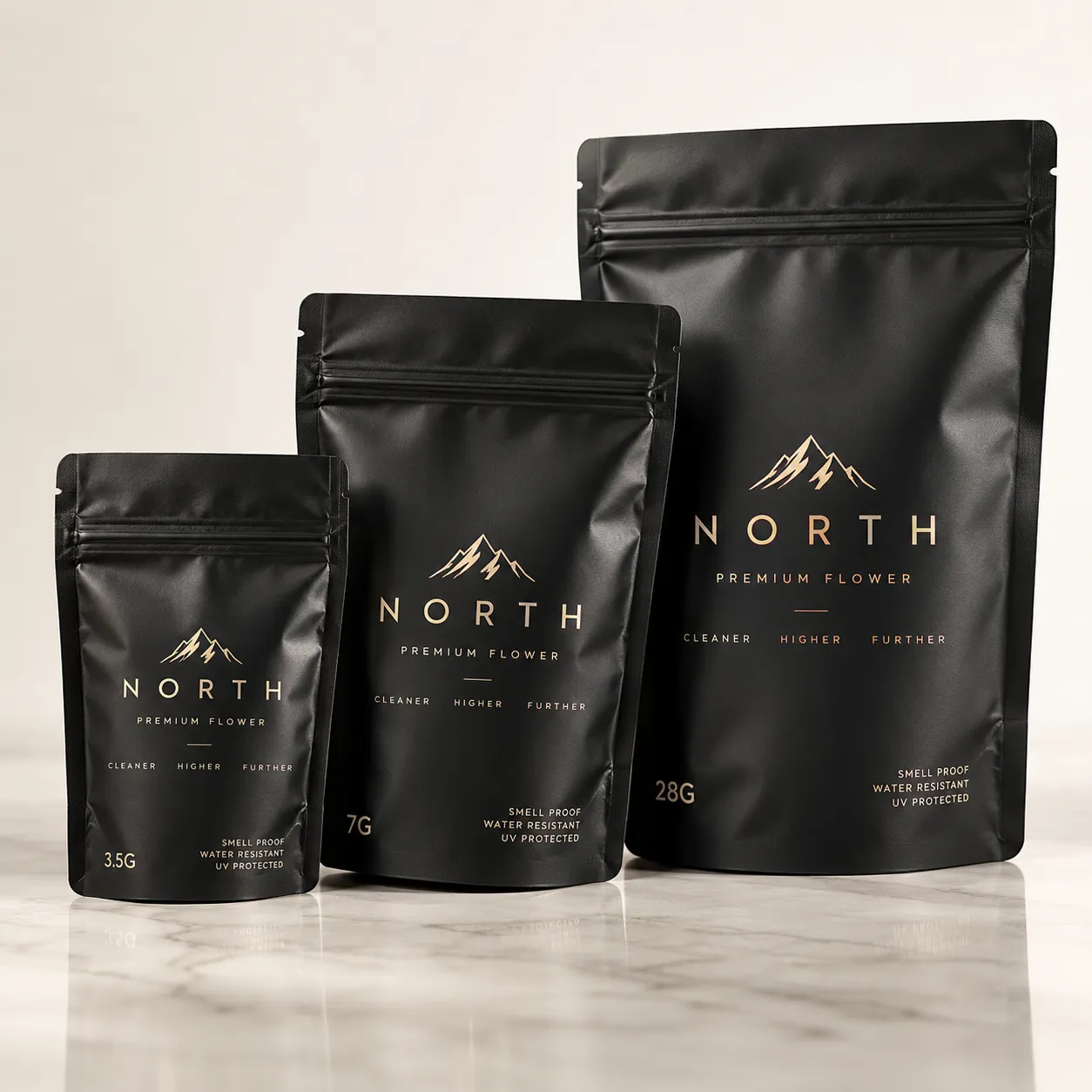 Three black matte cannabis mylar bags by North Premium Flower in 3.5g, 7g, 28g sizes with gold mountain logo on marble